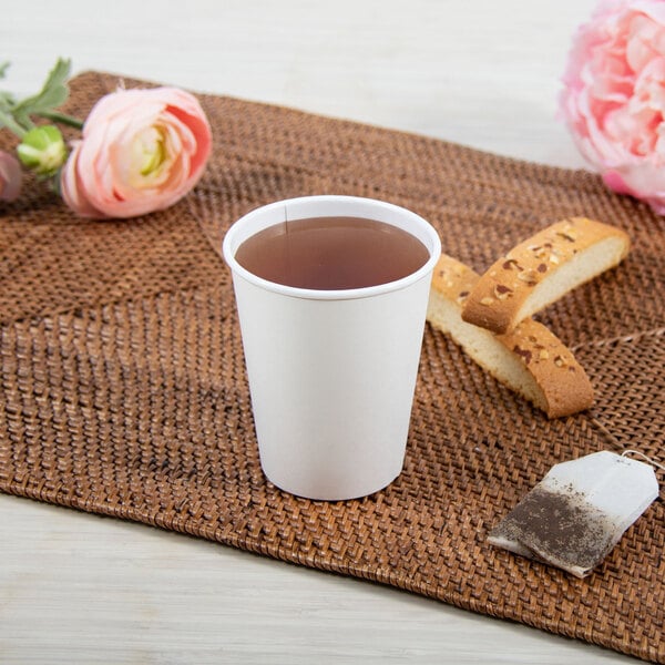 A Dart ThermoGuard white paper hot cup with tea and a tea bag on a table.