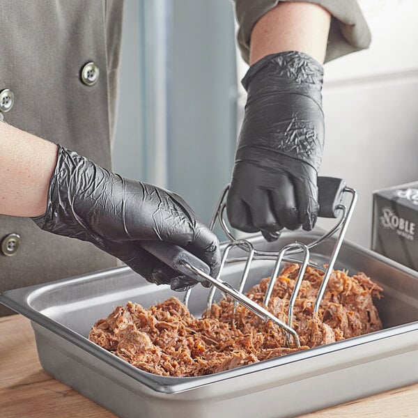 A person in black Noble disposable gloves using tongs to serve food in a container.