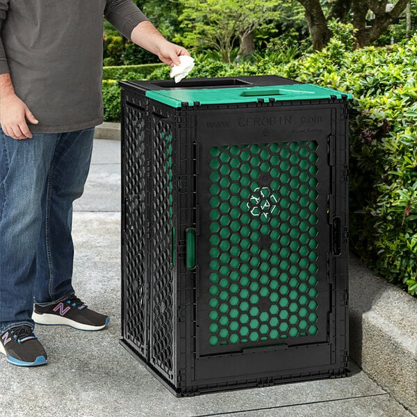 A man using a black Cerobin trash can with green hexagons to throw away paper.