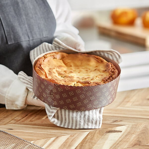 A person holding a baked dish in a brown paper Novacart baking mold.