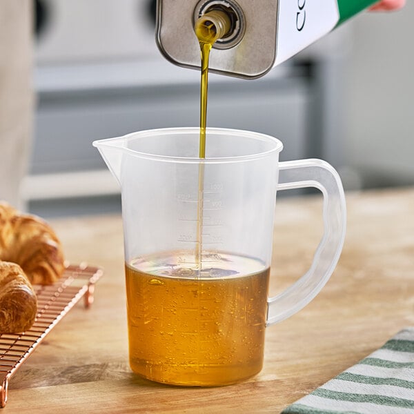 A person pouring brown liquid into an Araven clear polypropylene measuring cup.