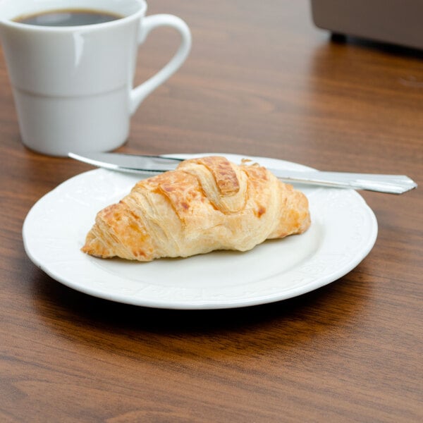 A Tuxton Chicago bright white china plate with a croissant and a cup of coffee on it.