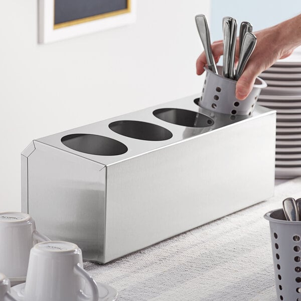 A person holding a stainless steel flatware organizer with utensils.