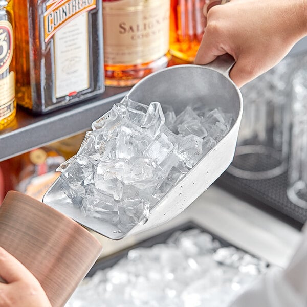 A person using a Choice aluminum scoop to pour ice into a brown cup.