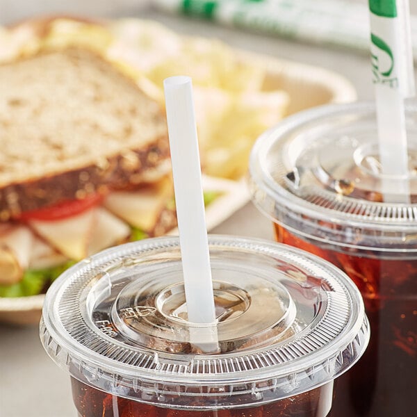 A plastic cup with a straw in a plastic lid on a table with a sandwich in a white container.