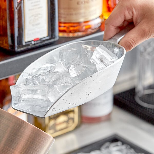 A hand holding a Choice flat bottom aluminum scoop filled with ice cubes.