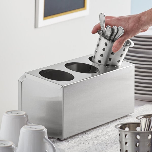 A hand holding a stainless steel flatware organizer with spoons inside.