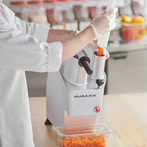 A person in a white coat and gloves using an AvaMix food processor to dice carrots.