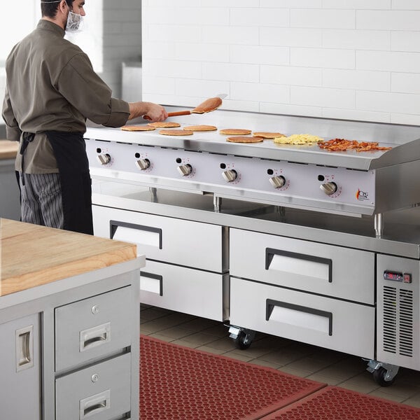 A man in a kitchen preparing food on a large stainless steel Cooking Performance Group chef base with a gas griddle.