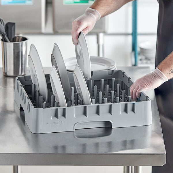 A person in a black apron is using a Cambro Soft Gray Camrack Peg Rack to clean plates.