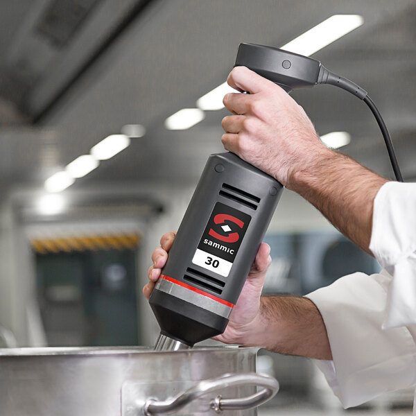 A person using a Sammic medium-duty immersion blender in a black and grey container.