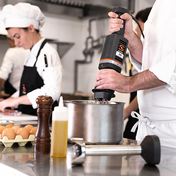 A chef using a Sammic medium-duty immersion blender with a whisk attachment in a professional kitchen.