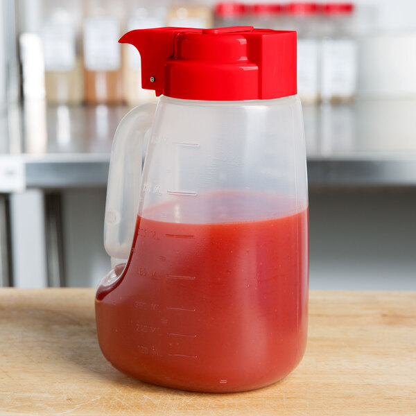 A Tablecraft plastic dispenser jar with a red lid on a counter.