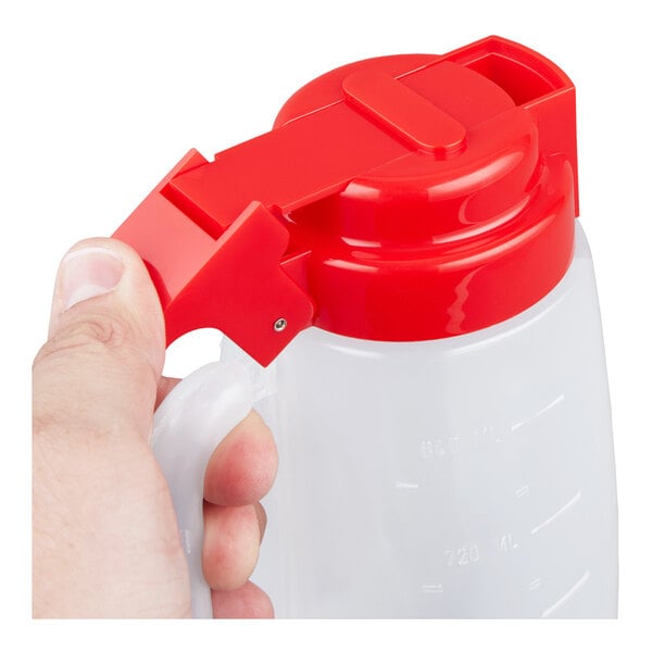 A 32 oz. plastic dispenser jar with a red lid and handle, being held by a hand.