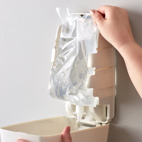 A hand putting a plastic bag of Noble Chemical Novo Pro Series foaming hand sanitizer into a dispenser.