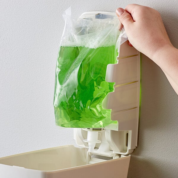 A hand holding a white bag of green liquid soap.