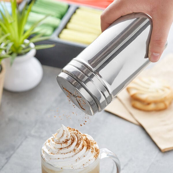 A hand using a Choice stainless steel shaker to sprinkle a drink.