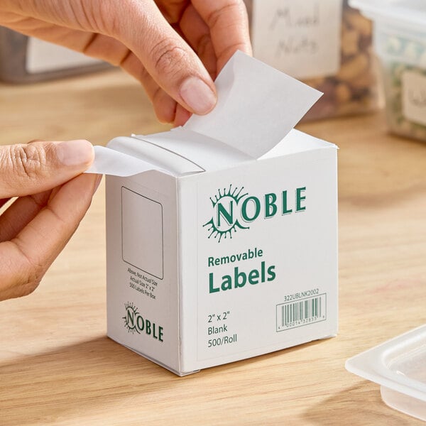 A box of Noble 2" x 2" removable blank labels containing 500 labels per roll.