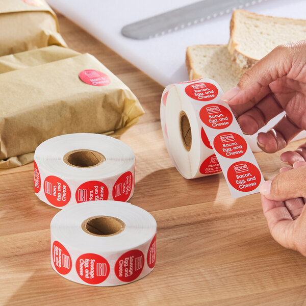 A roll of red permanent labels reading 'Bacon, Egg, and Cheese' used for food packaging.