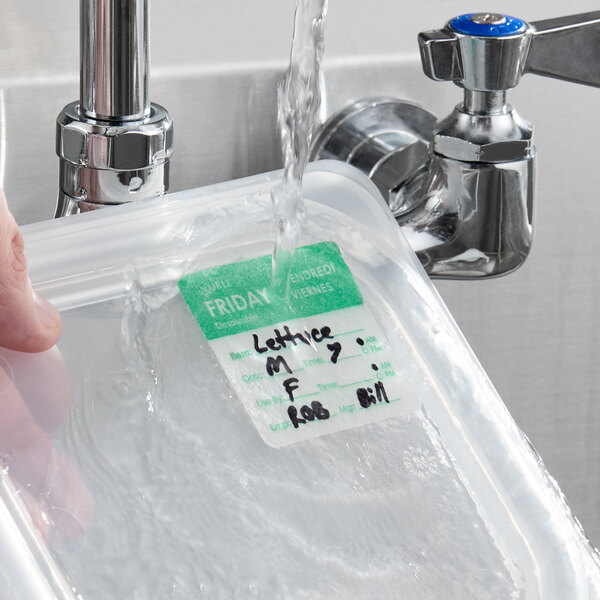 A dissolvable day of the week label marked for Friday, adhered to a plastic container under running water.