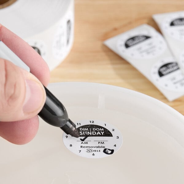 A round removable day of the week clock label marked for Sunday being written on with a black marker.