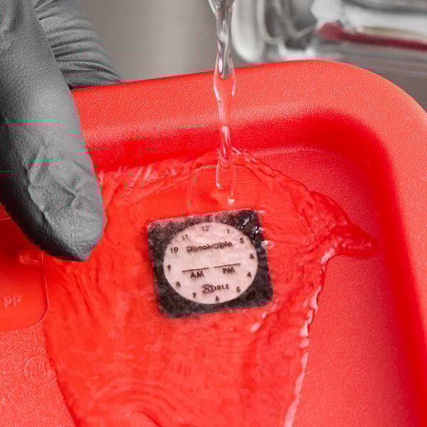 A dissolvable clock label being rinsed with water in a red container.
