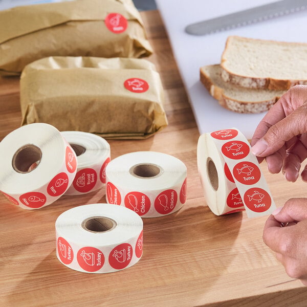 A roll of red circular labels with white illustrations and text for identifying sandwich contents such as turkey, tuna, chicken, and beef.