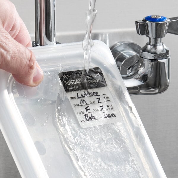 A dissolvable day of the week label being washed off a food container under running water.