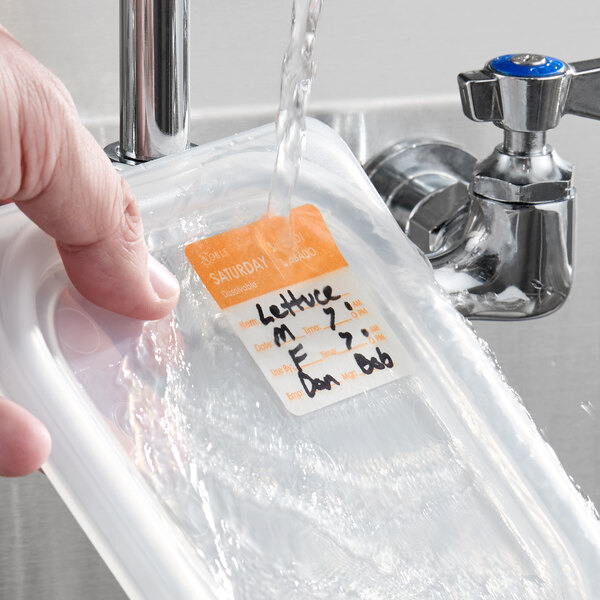 A dissolvable day of the week label being washed off a food container under running water.