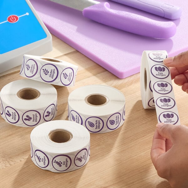 A set of rolls of purple allergen labels, including tree nuts, gluten, and egg allergen warnings, on a wooden surface.