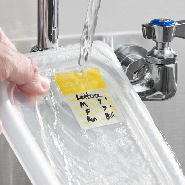 A dissolvable day of the week label with Tuesday highlighted, attached to a food container being rinsed under running water.