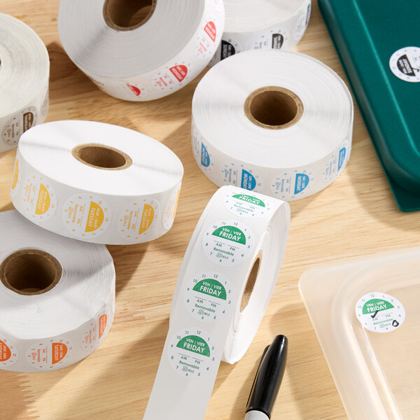 A collection of Noble 1-inch removable day of the week clock label rolls in various colors on a wooden surface.