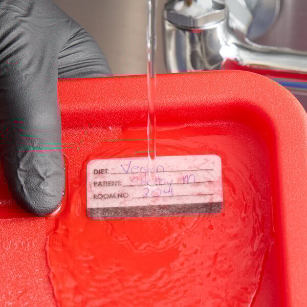 A dissolvable hospital label being rinsed off a red container under running water.