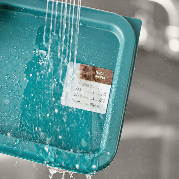 A blue container of Noble Products Thursday food labeling stickers with water being poured over it.