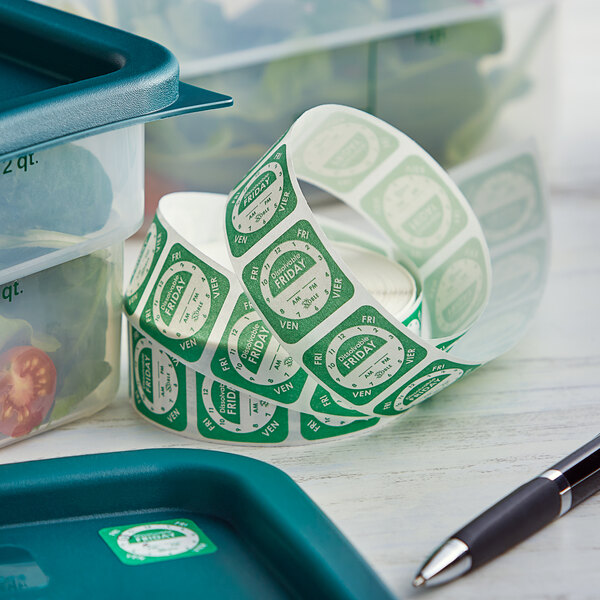 A roll of Noble Products Friday dissolvable day of the week stickers next to a green container and a pen.