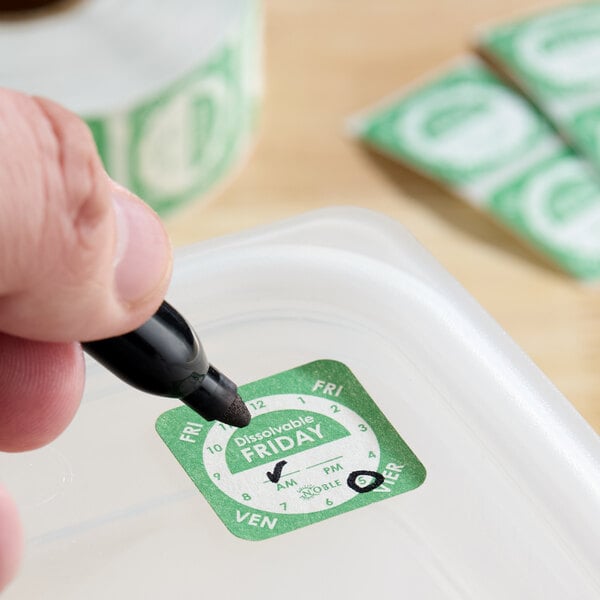 A dissolvable Friday day-of-the-week clock label being written on and applied to a plastic food container.