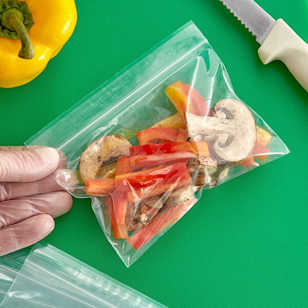 A hand using a Clear Line plastic bag to hold a yellow pepper and mushrooms.