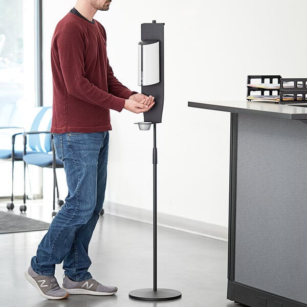 A man standing in front of a white metal Lavex foaming soap stand.