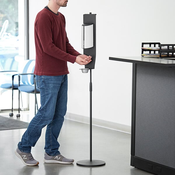 A man standing in front of a Lavex white metal automatic soap and sanitizer station.