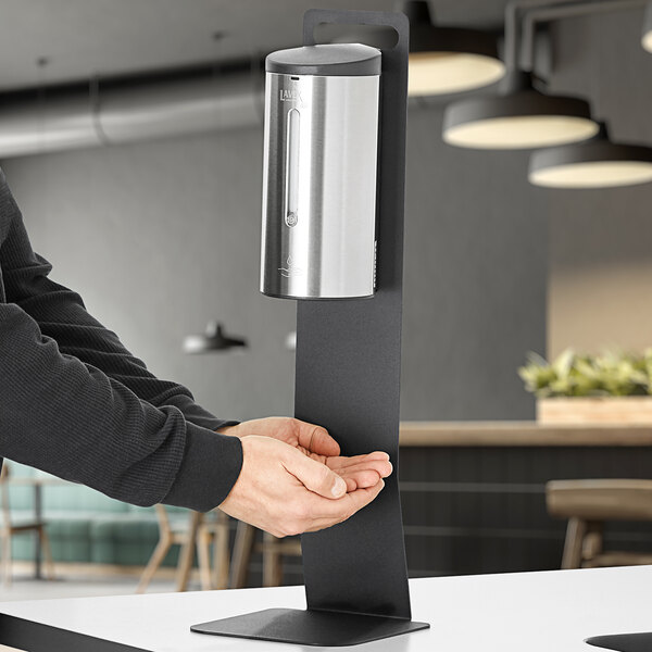 A person using a Lavex stainless steel table top foaming soap dispenser.