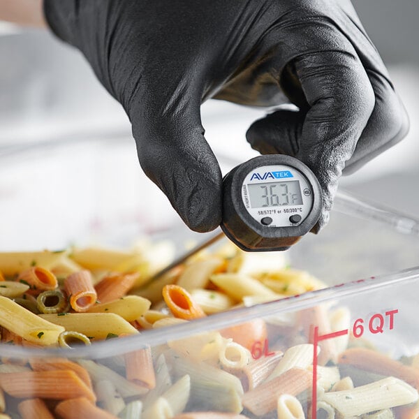 A person in black gloves using an AvaTemp digital pocket probe thermometer to check pasta temperature.
