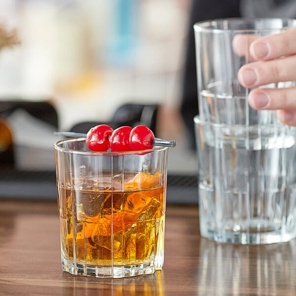A hand holding a Duralex Jazz Rocks glass with a drink and a cherry on top.