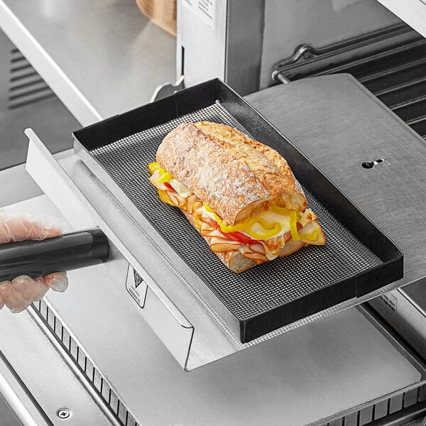 A Baker's Mark non-stick mesh basket holding a sandwich with meat and vegetables.