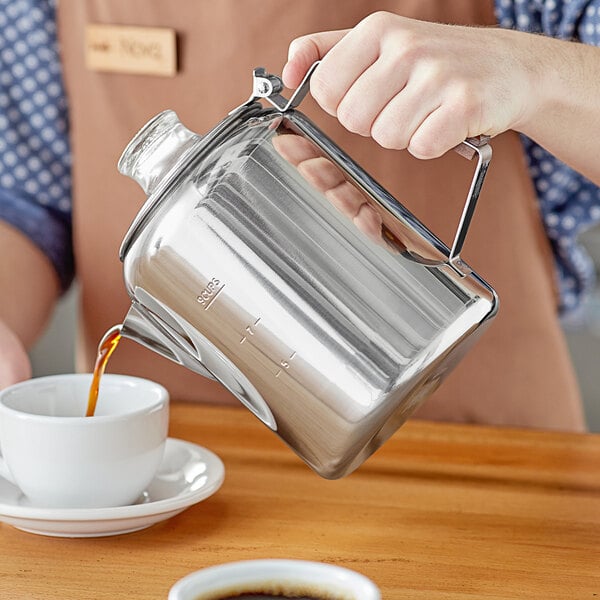 A person using a Fox Run stainless steel stovetop percolator to pour coffee into a cup.