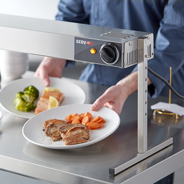 A person using a ServIt strip warmer to serve a plate of meat and carrots.