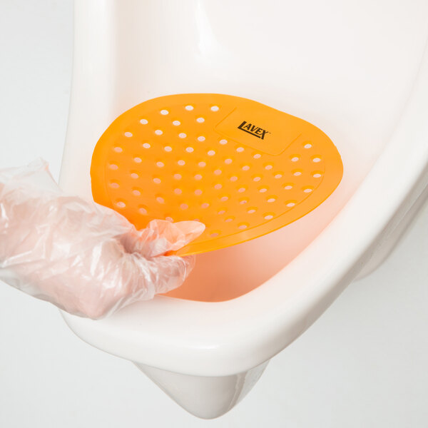 A gloved hand placing a Lavex Citrus Scent Deodorized Urinal Screen in a urinal.
