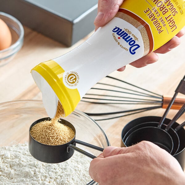 A hand pouring Domino brown sugar from a flip-top container.