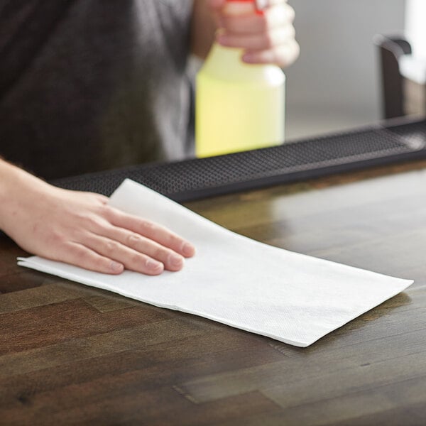 A person using a Chicopee Chix foodservice towel to clean a table in a professional kitchen.