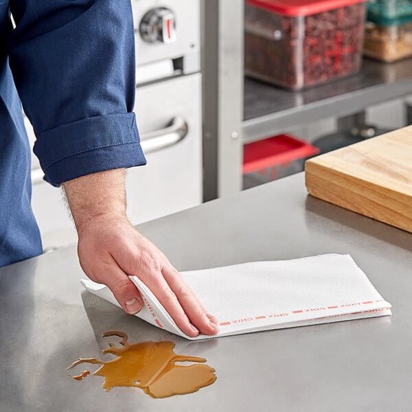 A hand wiping a table with a white and red Chicopee foodservice towel.