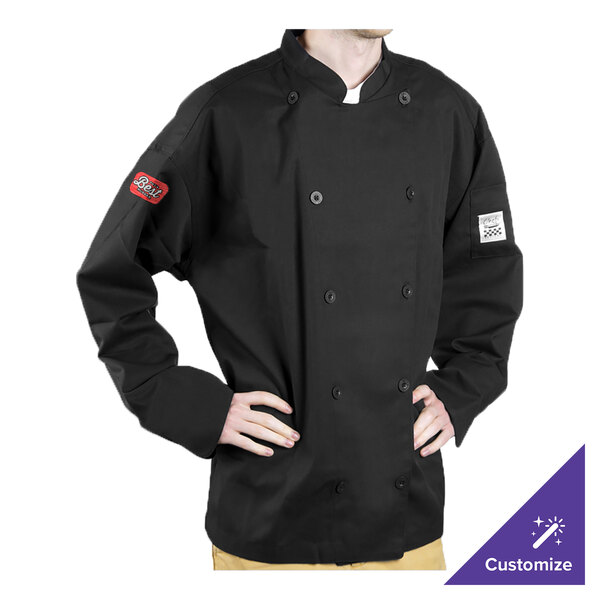 A person wearing a black Chef Revival long sleeve chef coat on a counter in a professional kitchen.